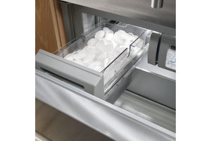 Primer plano de una gaveta de frigorífico de acero inoxidable con un depósito de hielo transparente lleno de hielo, que se muestra parcialmente abierto.