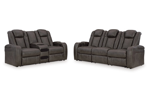 Juego de sala reclinable gris oscuro, compuesto por loveseat con consola central y sofá de tres asientos, con respaldos acolchados, detalles capitonados, brazos anchos, costuras claras y paneles laterales texturizados sobre fondo blanco, con luces LED sobre un fondo blanco. 