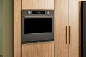 Horno empotrado de acero inoxidable con puerta de cristal negro y panel de control digital, integrado en armarios de cocina de madera de roble claro.