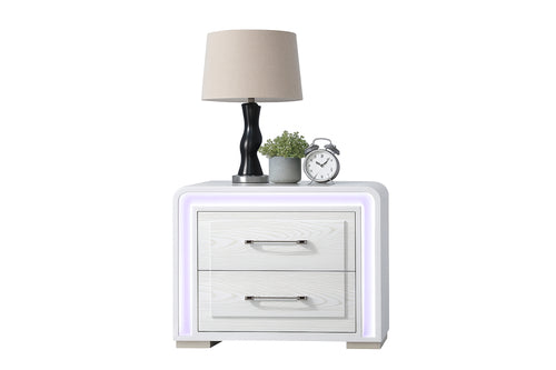 Mesa de noche de color blanco con dos gavetas, luces LED, y elementos decorativos encima de la mesa sobre un fondo blanco. 