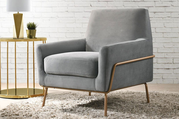 Silla de acento de color gris con una base metálica dorada en una sala neutral con objetos decorativos. 