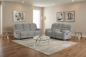 Juego de sala reclinable en tela gris claro compuesto por sofá y loveseat. Presentado en una sala luminosa con ventanas amplias, mesa de centro redonda y decoración moderna en tonos neutros para un ambiente acogedor.