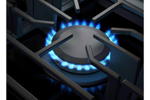 Primer plano de un quemador de estufa de gas con una rejilla de metal oscuro y una llama azul brillante encendida debajo de la tapa del quemador.