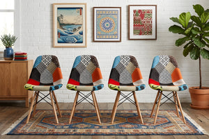 Cuatro sillas coloridas dispuestas en fila sobre una alfombra estampada, con cuadros enmarcados y una planta al fondo.