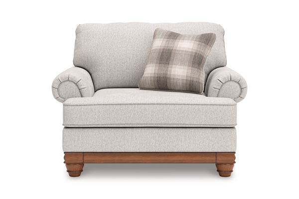 Silla de acento de color beige con brazos y un cojín decorativo sobre un fondo blanco. 