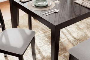 Mesa de comedor de madera oscura con sillas tapizadas en gris en un ambiente moderno, decorada con vajilla y una alfombra con diseño.