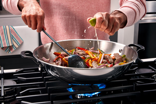 Persona cocinando un salteado en un wok sobre una estufa de gas.