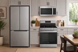 Una escena de cocina moderna que incluye una nevera de acero inoxidable con puertas francesas, una estufa de gas de acero inoxidable a juego y un microondas de acero inoxidable montado sobre la estufa, todo ello sobre gabinetes de color gris claro.