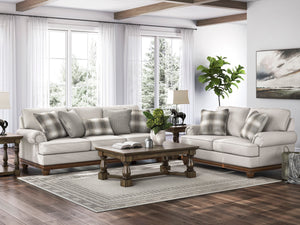 Juego de sala tradicional con sofá y loveseat en color beige claro, cojines decorativos a rayas y bases de madera oscura, acompañado de una mesa de centro de madera tallada sobre una alfombra neutra en una sala luminosa con grandes ventanas.