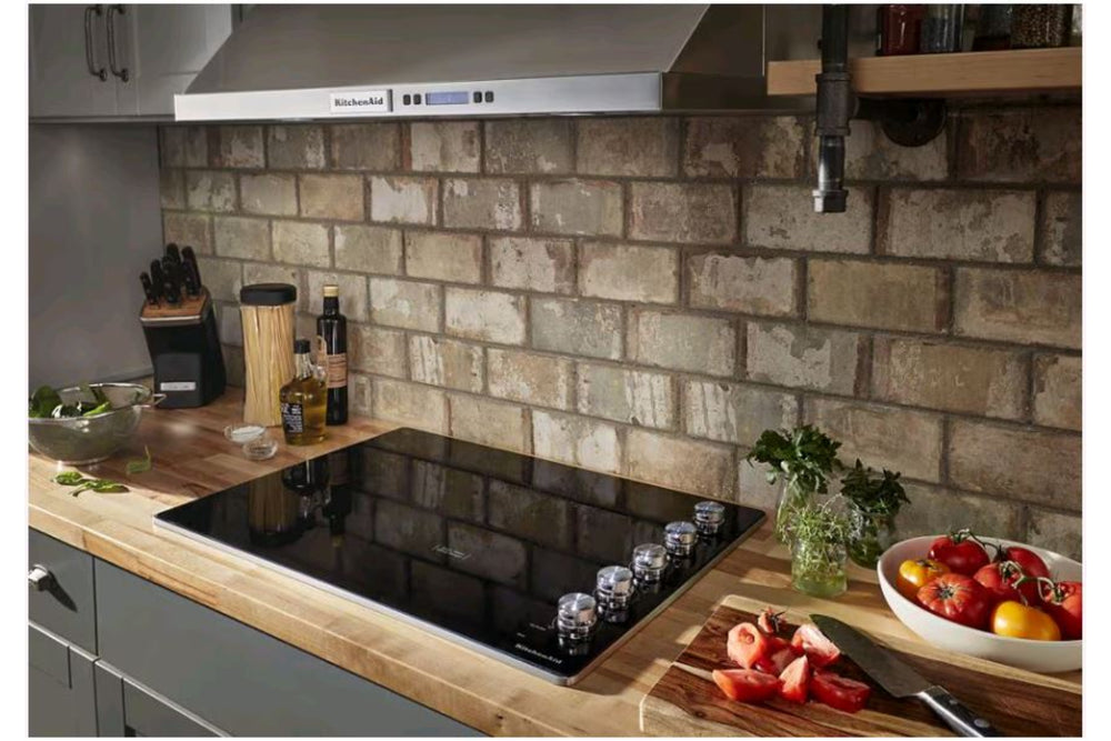Tope KitchenAid con superficie vitrocerámica negra, cinco zonas de cocción eléctricas y controles giratorios laterales. Diseño moderno y elegante ideal para cocinas contemporáneas y espacios integrados.