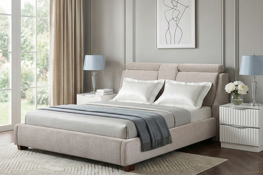Cama tapizada en tela color beige con cabecera acolchada de diseño moderno y detalle central decorativo. Incluye estructura baja con patas de madera visibles y colchón de perfil bajo, ideal para dormitorios contemporáneos.