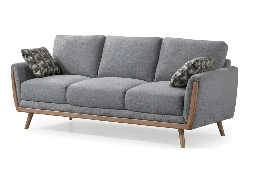 Un sofá de tres asientos tapizado en gris con estructura de madera clara y patas cónicas, decorado con dos almohadas decorativas estampadas sobre un fondo blanco.