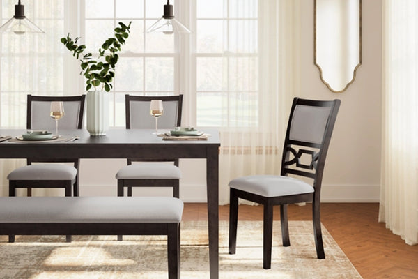 Un juego de comedor que incluye una mesa rectangular de madera oscura, un banco a juego con asiento tapizado en gris claro y tres sillas con estructura de madera oscura y asientos tapizados en gris claro, en un espacio luminoso con grandes ventanas y cortinas traslúcidas.