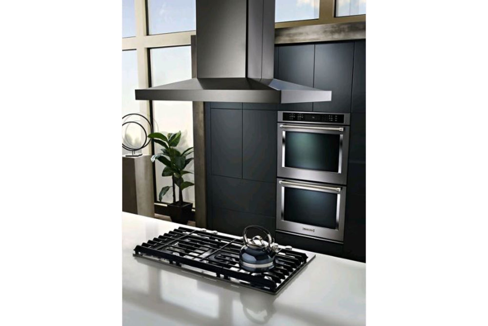 Campana extractora KitchenAid de pared en acero inoxidable con diseño tipo chimenea, iluminación LED integrada y controles electrónicos frontales. Ideal para eliminar humo, olores y vapores en cocinas modernas.