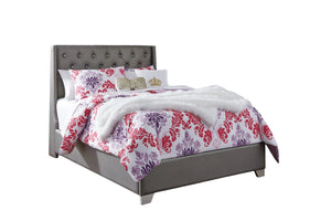 Cama con edredón estampado de flores y cabecero gris sobre fondo blanco.