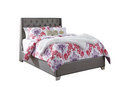 Cama con edredón estampado de flores y cabecero gris sobre fondo blanco.