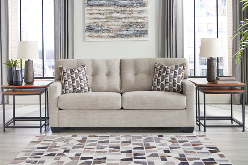 Sofá de color beige con cojines decorativos con patas acabadas en una sala moderna con elementos decorativos. 