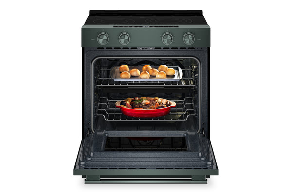 Un horno eléctrico independiente con exterior de color verde y puerta abierta, que deja ver dos rejillas con comida en su interior: una bandeja con pequeños panecillos dorados en la parte superior y una fuente roja para hornear en la parte inferior.