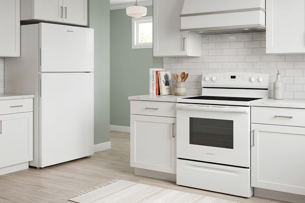 Cocina moderna con nevera de congelador superior y estufa eléctrica blanca de cuatro quemadores, instalada entre gabinetes blancos y salpicadero de azulejos tipo subway en color blanco.