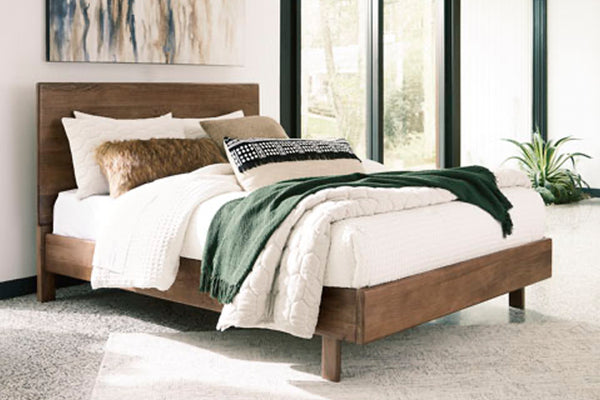 Cama de madera con ropa de cama blanca y manta verde en una habitación con grandes ventanales.