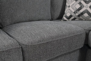 Primer plano de un cojín de sofá de tela texturizada gris con un cojín decorativo estampado parcialmente visible a la derecha.