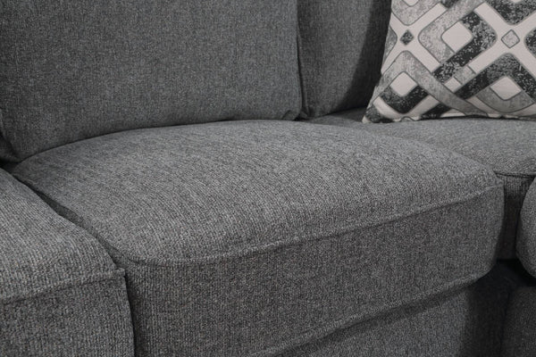 Primer plano de un cojín de sofá de tela texturizada gris con un cojín decorativo estampado parcialmente visible a la derecha.