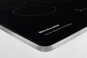 Primer plano de un tope de inducción negro con esquinas redondeadas, un borde de metal plateado cepillado y el logotipo de KitchenAid impreso en la superficie.