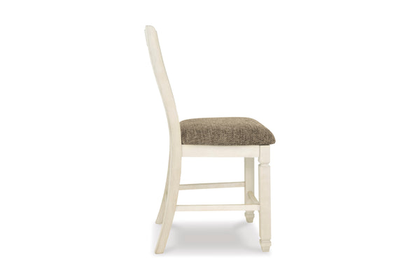 Una silla de comedor individual vista de perfil sobre un fondo blanco liso. La silla tiene una estructura de madera pintada en color blanco roto con aspecto envejecido y un cojín de asiento tapizado en color marrón topo texturizado.