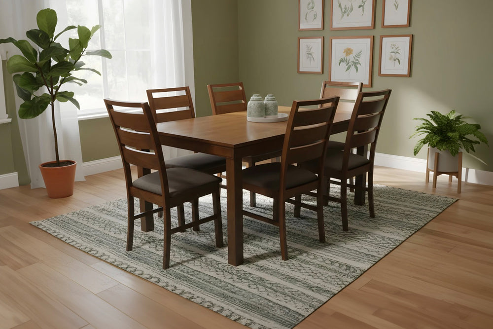 Comedor con mesa y sillas de madera marrón sobre una alfombra a rayas, plantas y cuadros enmarcados en la pared.