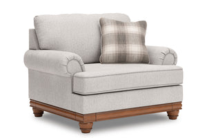 Vista lateral de silla de acento de color beige con brazos y un cojín decorativo sobre un fondo blanco. 