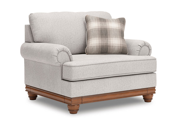 Vista lateral de silla de acento de color beige con brazos y un cojín decorativo sobre un fondo blanco. 