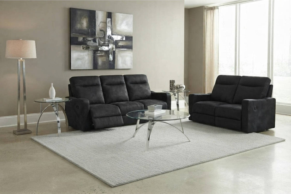 Un salón moderno con un sofá reclinable negro de tres plazas y un sillón reclinable de dos plazas a juego sobre una alfombra gris clara. Tiene paredes beige, mesa de centro de cristal, lámpara de pie y un cuadro abstracto grande.