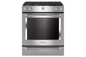 Una estufa independiente de acero inoxidable con placa de cocción de vidrio negro, cinco perillas de control, una gran ventana en el horno y un cajón de almacenamiento inferior, mostrada sobre un fondo blanco liso.