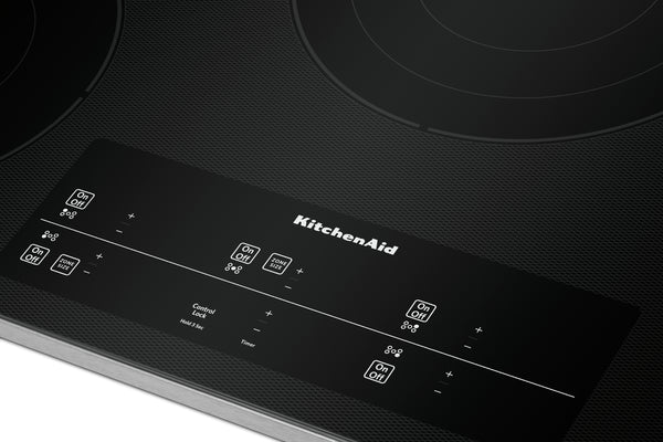 Primer plano de un tope de inducción KitchenAid negro con un panel de control brillante e iconos blancos impresos sobre una superficie oscura texturizada.