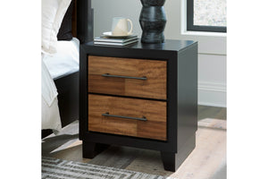 Mesa de noche de madera y color negro con dos gavetas en ambiente de habitación. 