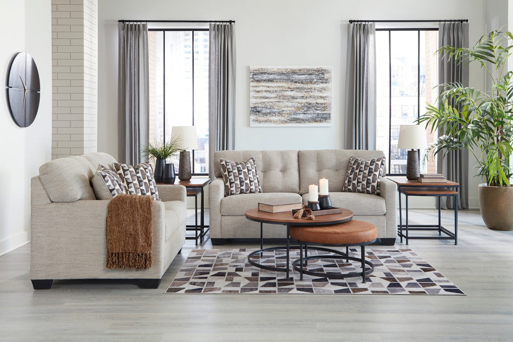 Loveseat y sofás beige con cojines estampados sobre un fondo blanco.