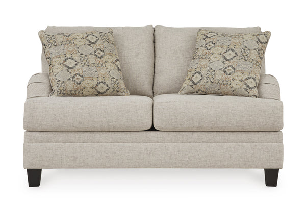 Loveseat beige con dos cojines decorativos sobre un fondo blanco. 