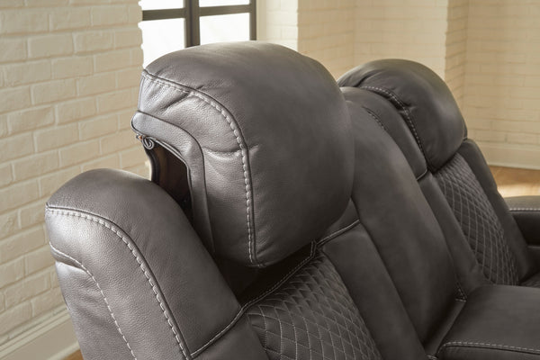 Loveseat reclinable gris con diseño acolchado contra una pared de ladrillos.