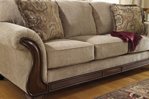 Sofá beige con cojines decorativos y una manta sobre suelo de madera.