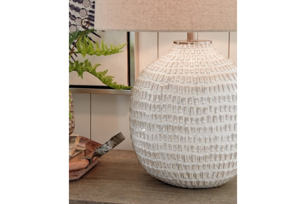 Lámpara de sobremesa con base de cerámica texturizada y pantalla de color beige sobre fondo blanco.