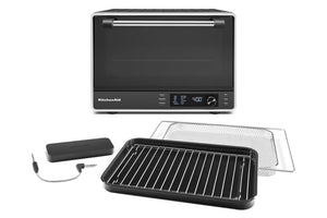 Horno de convección de sobremesa KitchenAid en color negro y acero inoxidable, que se muestra con una bandeja negra, una rejilla metálica y un termómetro digital con sonda sobre un fondo blanco.