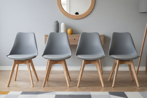 Cuatro sillas grises claras con patas de madera dispuestas en fila contra una pared de color neutro.