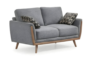 Un loveseat biplaza moderno de tela gris con detalles en madera clara y patas cónicas, decorado con dos cojines estampados sobre un fondo blanco.