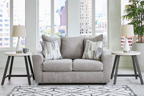 Loveseat de color gris con cojines decorativos y con elementos decorativos en una sala con ventanas en el fondo. 