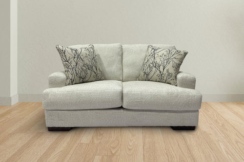 Loveseat de color beige con cojines decorativos en una sala neutral. 