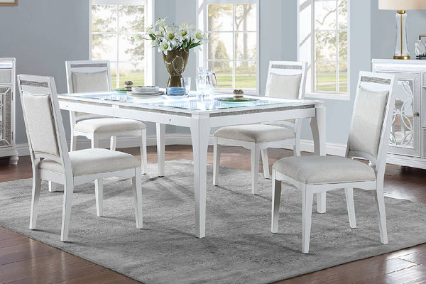 Mesa blanca con cuatro sillas con acolchado crema en un sala de comedor con objetos decorativos. 