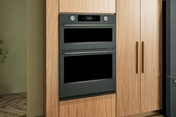Horno doble empotrado con acabado metálico verde y puertas de cristal, integrado en un mueble de madera de roble claro.