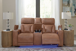 Loveseat reclinable en color café claro con consola central abatible, portavasos iluminados, controles laterales y luz LED azul en la base, ubicado entre dos mesas auxiliares con lámparas decorativas.