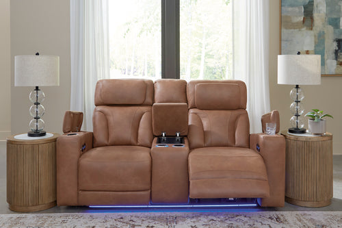 Loveseat reclinable en color café claro con consola central abatible, portavasos iluminados, controles laterales y luz LED azul en la base, ubicado entre dos mesas auxiliares con lámparas decorativas.
