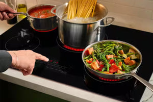 Persona cocinando en una estufa con ollas de pasta, verduras y sopa.